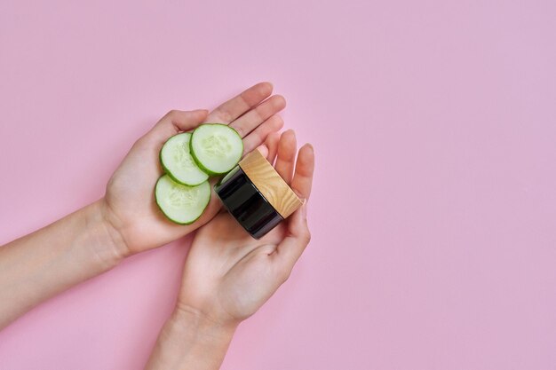 Vrouwenhanden met plakjes komkommer in glazen fles op roze achtergrond