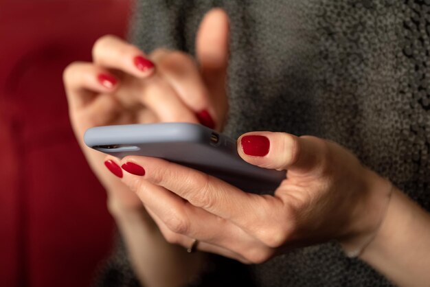 Vrouwenhanden met rode manicure die mobiele telefoon houden en sms'en