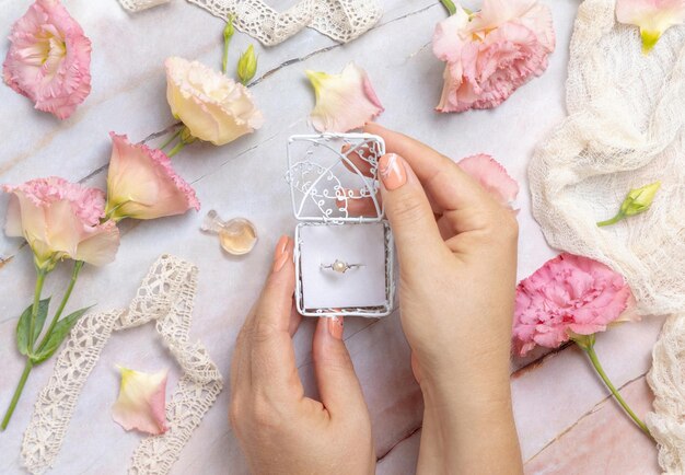 Vrouwenhanden openen een geschenkdoos met een parelring met lichtroze bloemen eromheen