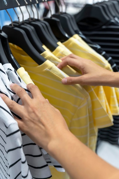 Vrouwenhanden sorteren T-shirts die aan een hanger in de winkel hangen