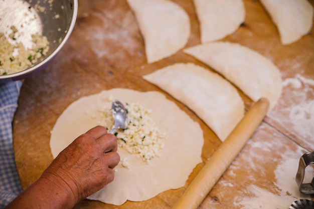 Vrouwenhanden tijdens het koken van kutaba of chebureks gehakt en uien in het deeg Cottage kaas en ui in het deeg Azerbeidzjaanse Tataarse Kaukasische Griekse keuken