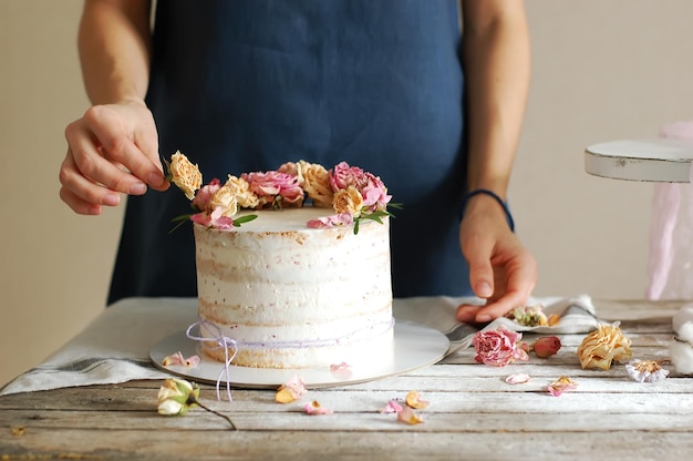 Vrouwenhanden versieren de slagroomtaart met verse bloemen. Horizontale foto.