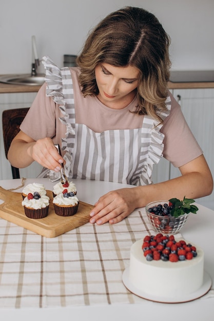 Vrouwenhanden versieren muffins met verse bosbessen en frambozen en muntblaadjes.