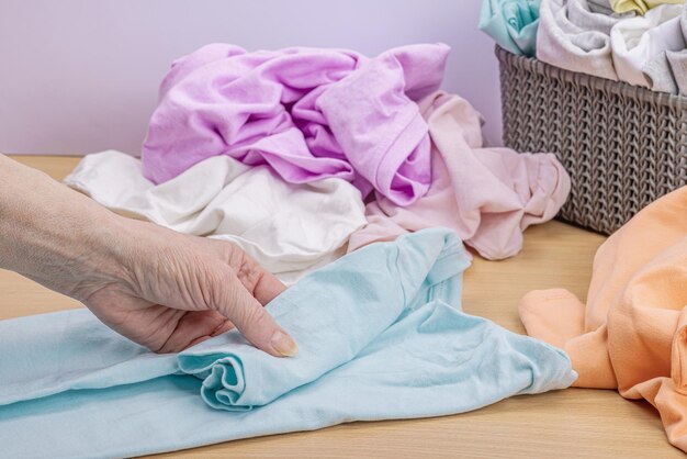 Vrouwenhanden vouwen schone kleding Verticale opslag van kleding in de manden Kast schoonmaken milieuvriendelijke stijl Pastelkleurige baby-T-shirts Lichte houten tafel kopieerruimte