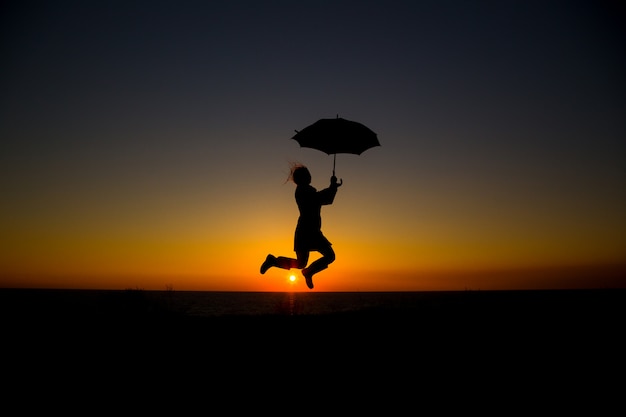 Foto vrouwenholding en paraplu in silhouet tegen oranje zonsondergang