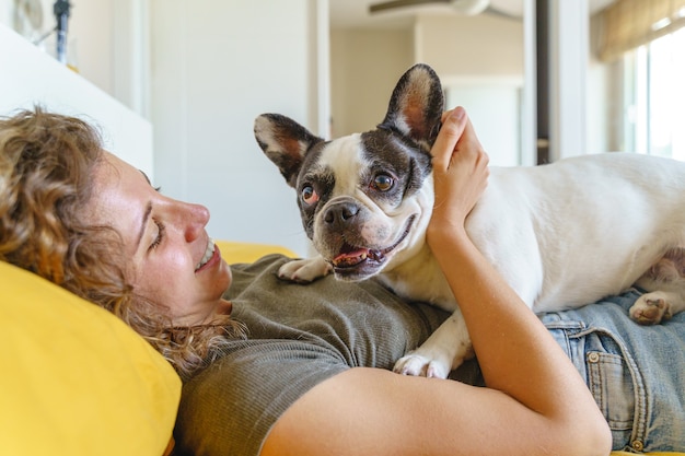 Vrouwenhondenliefhebber met buldog in bed. Zijaanzicht van vrouw spelen met huisdier. Levensstijl met dieren binnenshuis.