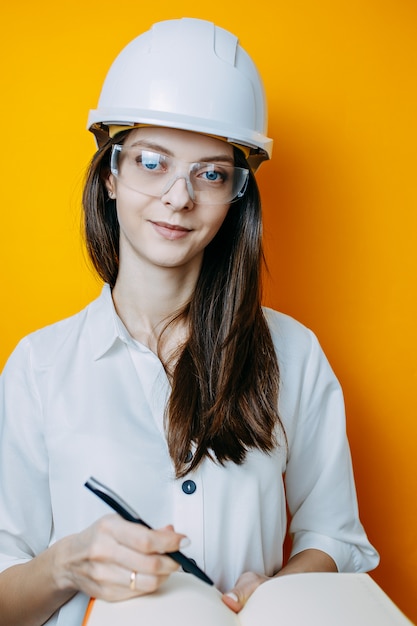 Vrouweningenieur in witte helm en glazen. Veiligheid poster. Vrouw in helm houdt notebook en pen.