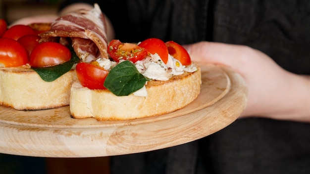 Vrouwenkelner die een houten dienblad met bruschetta met kersentomaten in haar hand houdt. Heerlijk Italiaans voorgerecht