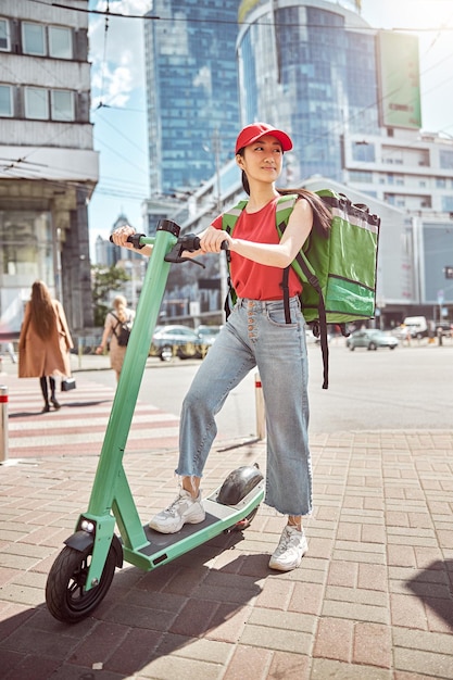 Vrouwenkoerier op elektrische scooter die voedsel door de stad levert