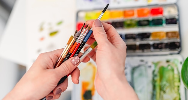 Vrouwenkunstenaarshanden die penselen vasthouden en er een kiezen om met waterverf te tekenen