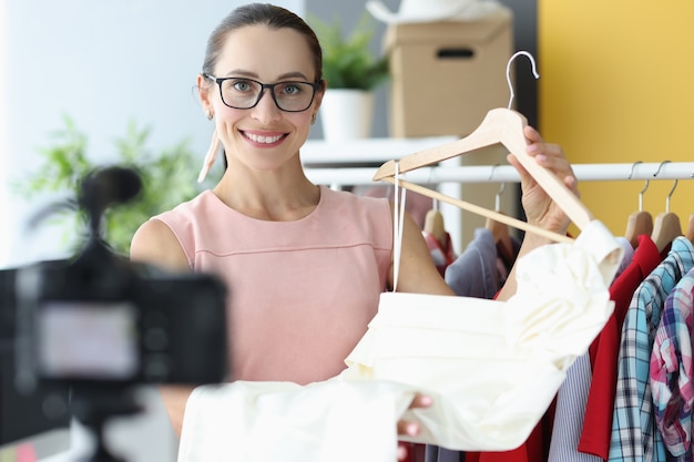 Vrouwennaad die witte kleding op hanger voor camera toont die kleren online concept verkopen