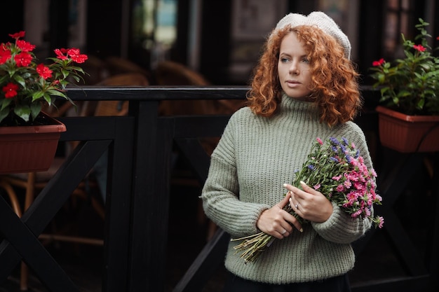 Vrouwenportret in een baret-sweater met een boeket bloemen van de achtergrond van het restaurant