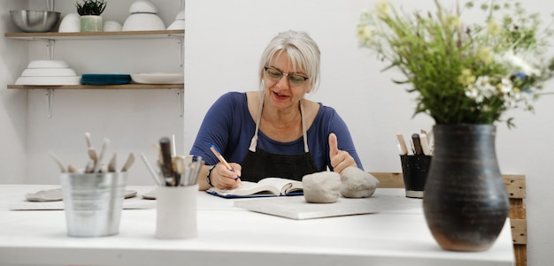 Vrouwenpottenbakker die bij de tafel schrijft Creatieve zaken plannen