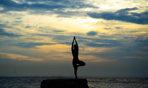 Vrouwensilhouet het praktizeren yoga bij kust