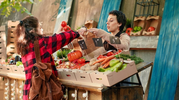 Vrouwenstandhouder die biologisch fruit en groenten aan klanten geeft en lokaal geteelde producten verkoopt op de lokale groentemarkt. Vrouwelijke groenteboer die natuurlijke bio verse producten toont. Schot uit de hand.