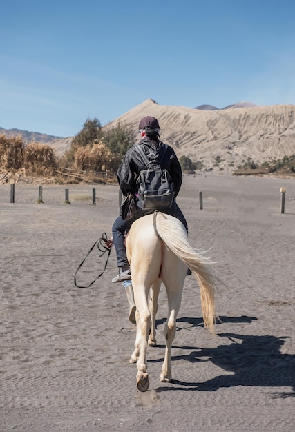 Vrouwentoerist die een wit paard berijdt op woestijn met vulkaan