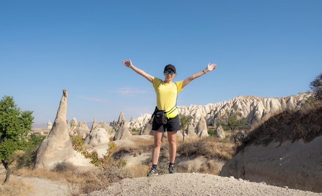 Vrouwentoerist die zich met opgeheven handen op de achtergrond van de Turkse bergen in Cappadocië bevindt