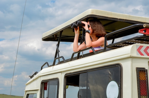 Vrouwentoerist op safari in Afrika, reis in Kenia, kijkend naar dieren in het wild in savanne met verrekijker