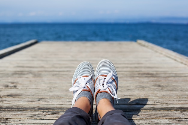 Vrouwenvoeten in vrijetijdsschoenen op de houten pier met zee- of oceaanachtergrond