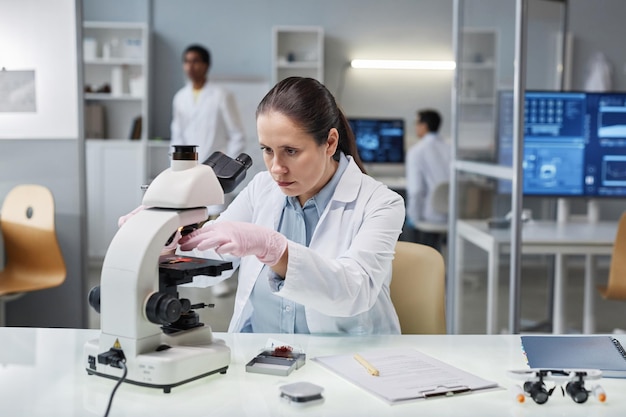 Vrouwenwetenschapper die testmateriaal in microscoop in laboratorium zetten