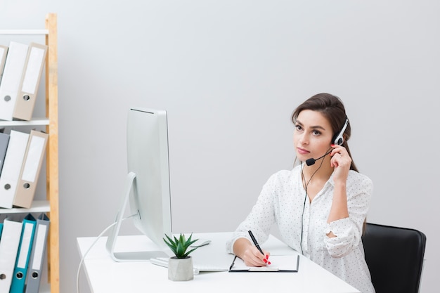 Vrouwenzitting bij bureau en het neerschrijven van iets terwijl het luisteren op hoofdtelefoon