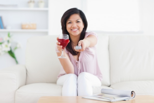 Vrouwenzitting in een witte laag terwijl het houden van een glas rode wijn en een verre televisie