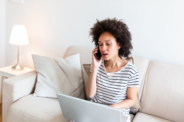 Vrouwenzitting op bank met laptop en thuis het spreken op telefoon.