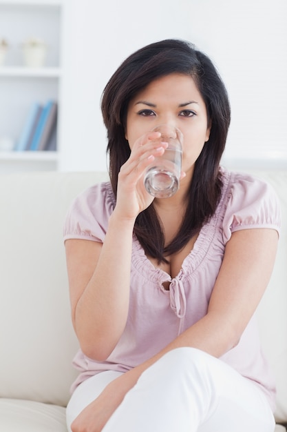 Vrouwenzitting op een laag terwijl het drinken van een glas water