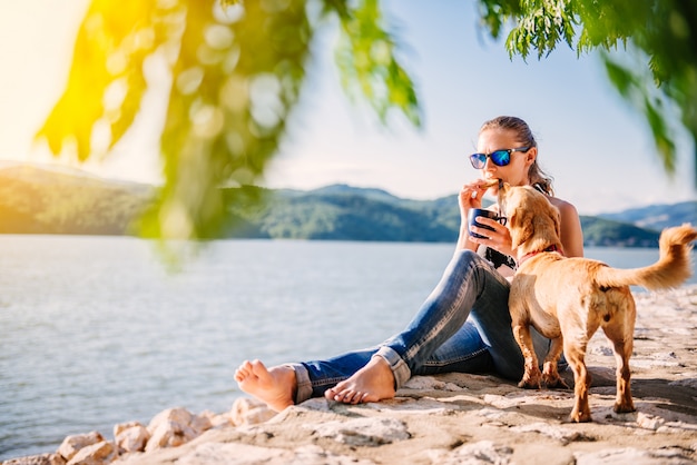 Vrouwenzitting op een strand met haar hond en het eten van koekjes