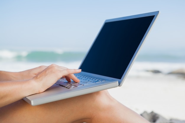 Vrouwenzitting op strand dat haar laptop met behulp van