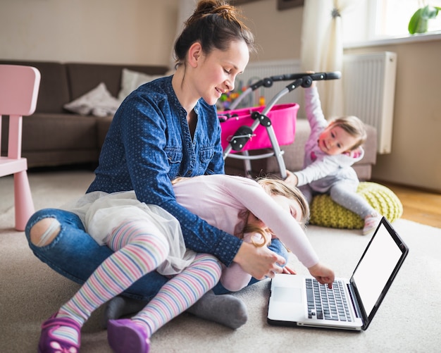 Foto vrouwenzitting op tapijt die meisje bekijken die laptop met behulp van