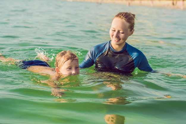 Vrouwenzweminstructeur voor kinderen leert een gelukkige jongen om in de zee te zwemmen