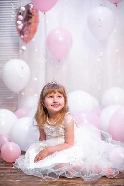 Vrouwtje, in feestelijke kleding en tiara, zit tegen ballonnen