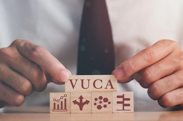 Vuca en strategisch management hand zet houten kubussen met vuca icoon en tekst vluchtigheid onzekerheid complexiteit ambiguïteit met grijze achtergrond slim management voor nieuwe trend en snelle transitie