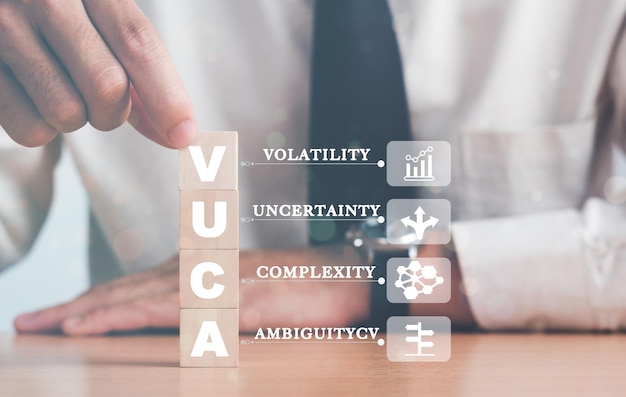 VUCA 및 전략적 관리 손은 VUCA 아이콘 및 텍스트 변동성이 있는 나무 큐브를 회색 배경으로 둡니다. 새로운 추세 및 빠른 전환을 위한 스마트 관리