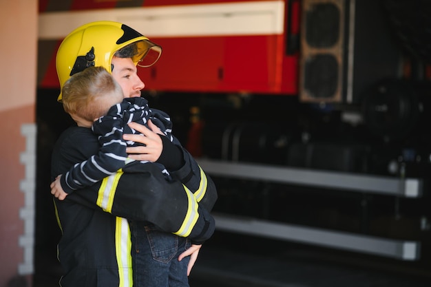 Vuile brandweerman in uniform met kleine geredde jongen die op zwarte achtergrond staat