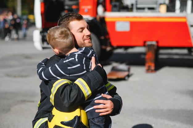 Vuile brandweerman in uniform met kleine geredde jongen die op zwarte achtergrond staat