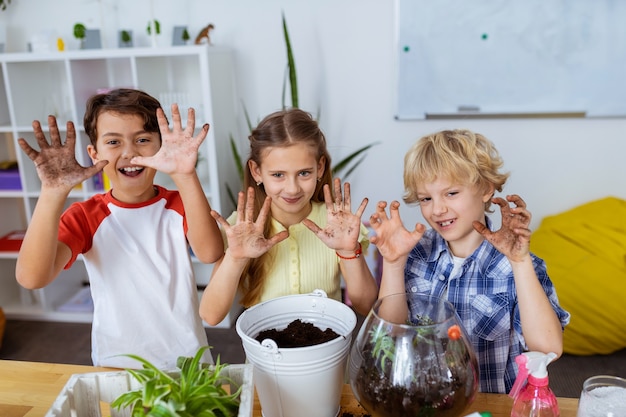 Vuile handen laten zien. Grappige leerlingen die hun vuile handen laten zien na het samen planten van de ecologieles