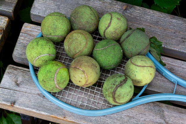 Vuile oude tennisballen en vintage tennisracket op houten bank Vrijetijdsactiviteiten buitenspellen