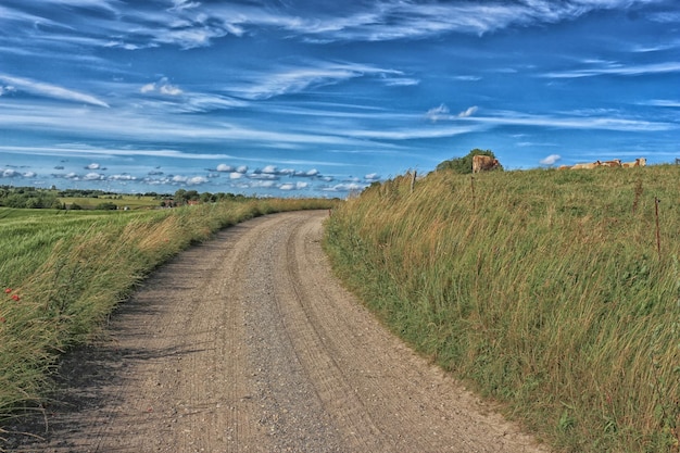 Vuilweg te midden van grasveld tegen bewolkte lucht
