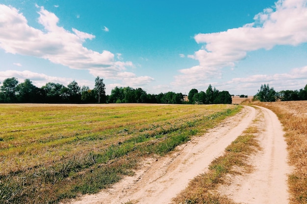 Vuilweg te midden van het veld tegen een bewolkte hemel