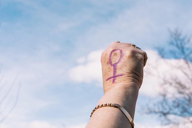 Vuist van een oudere vrouw met paars gelakte nagels met de lucht op de achtergrond met het vrouwelijke symbool geschilderd Concept van women39s day empowerment gelijkheid ongelijkheid activisme en protest