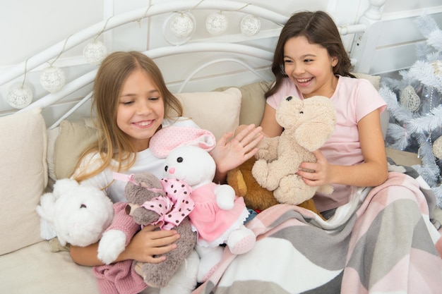 Vul uw kerst met vreugde Kleine meisjes spelen met speelgoed Kleine kinderen genieten van Kerstmis Kleine kinderen hebben Kerstmis plezier Gelukkige kinderen in bed bij de kerstboom Jeugdspelletjes op kerstmis en nieuwjaar