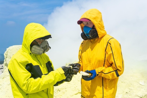 Vulkanologen op de helling van de vulkaan onderzoeken monsters van mineralen tegen de achtergrond van rokende zwavelfumarolen