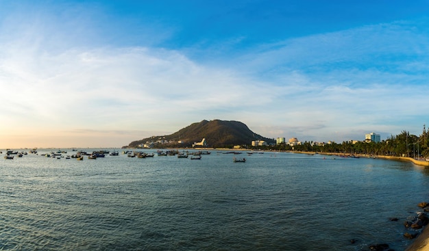 Vung Tau city aerial view with beautiful sunset and so many boats Panoramic coastal Vung Tau view from above with waves coastline streets coconut trees and Tao Phung mountain in Vietnam