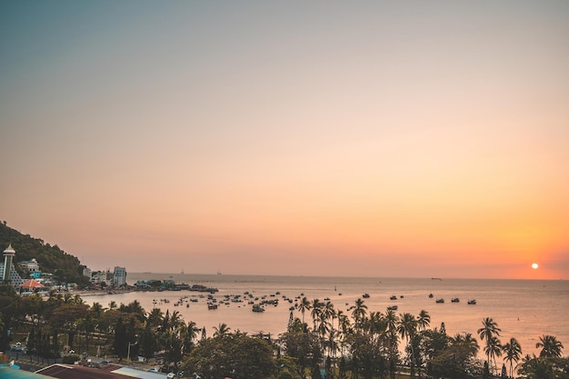 Vung Tau city aerial view with beautiful sunset and so many boats Panoramic coastal Vung Tau view from above with waves coastline streets coconut trees and Tao Phung mountain in Vietnam