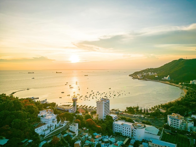 Vung Tau city aerial view with beautiful sunset and so many boats Panoramic coastal Vung Tau view from above with waves coastline streets coconut trees and Tao Phung mountain in Vietnam