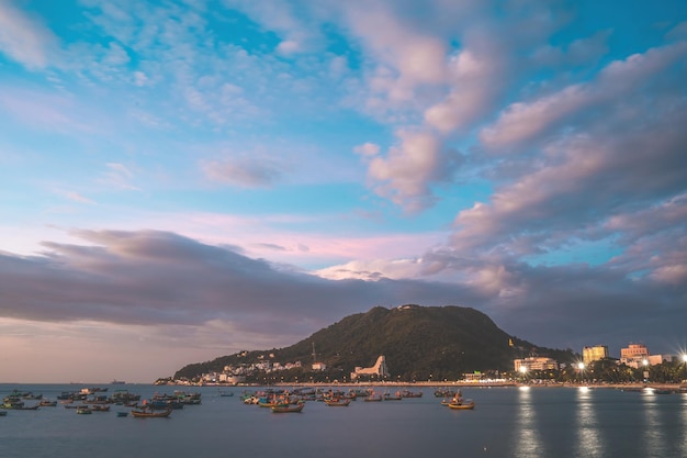 Vung Tau city aerial view with beautiful sunset and so many boats Panoramic coastal Vung Tau view from above with waves coastline streets coconut trees and Tao Phung mountain in Vietnam