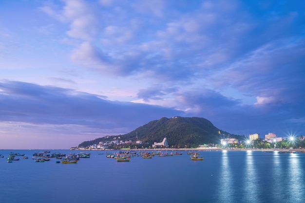 Vung Tau city aerial view with beautiful sunset and so many boats Panoramic coastal Vung Tau view from above with waves coastline streets coconut trees and Tao Phung mountain in Vietnam