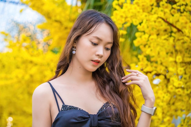 Vung Tau VIETNAM 7 JANUARI 2023 Portret van een mooie Aziatische vrouw in zwarte jurk staande in de buurt van Ochna Integerrima bloem Tet vakantie Lunar New Year